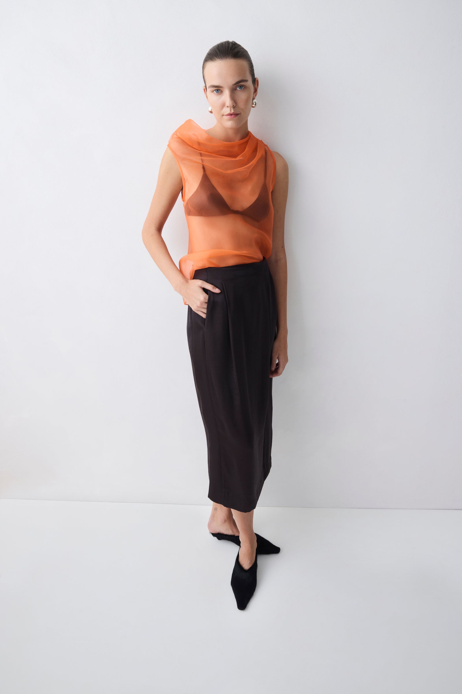 Woman wearing an orange sleeveless top and black skirt against a white background