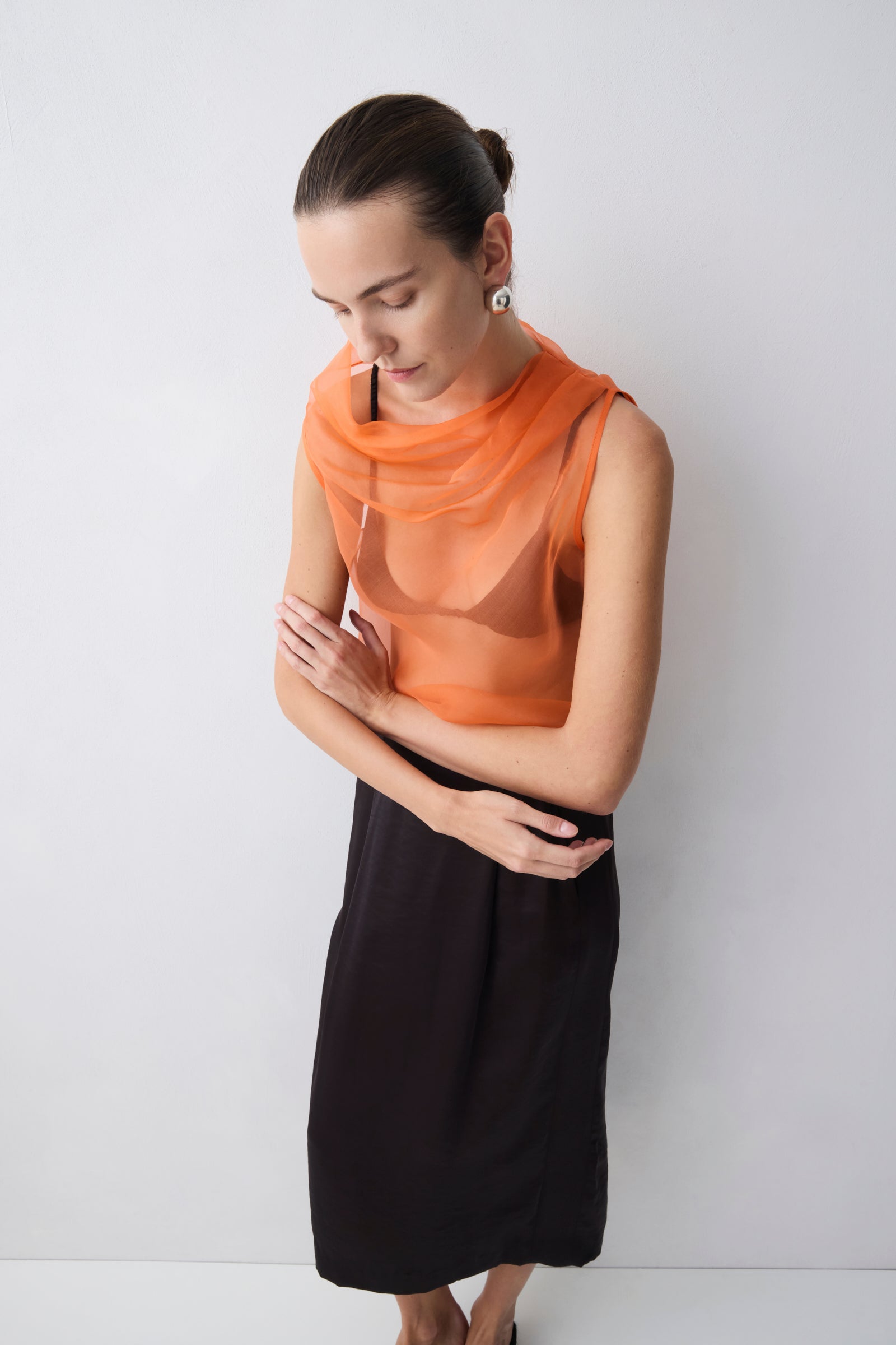 Woman wearing an orange sheer top and black skirt against a white background
