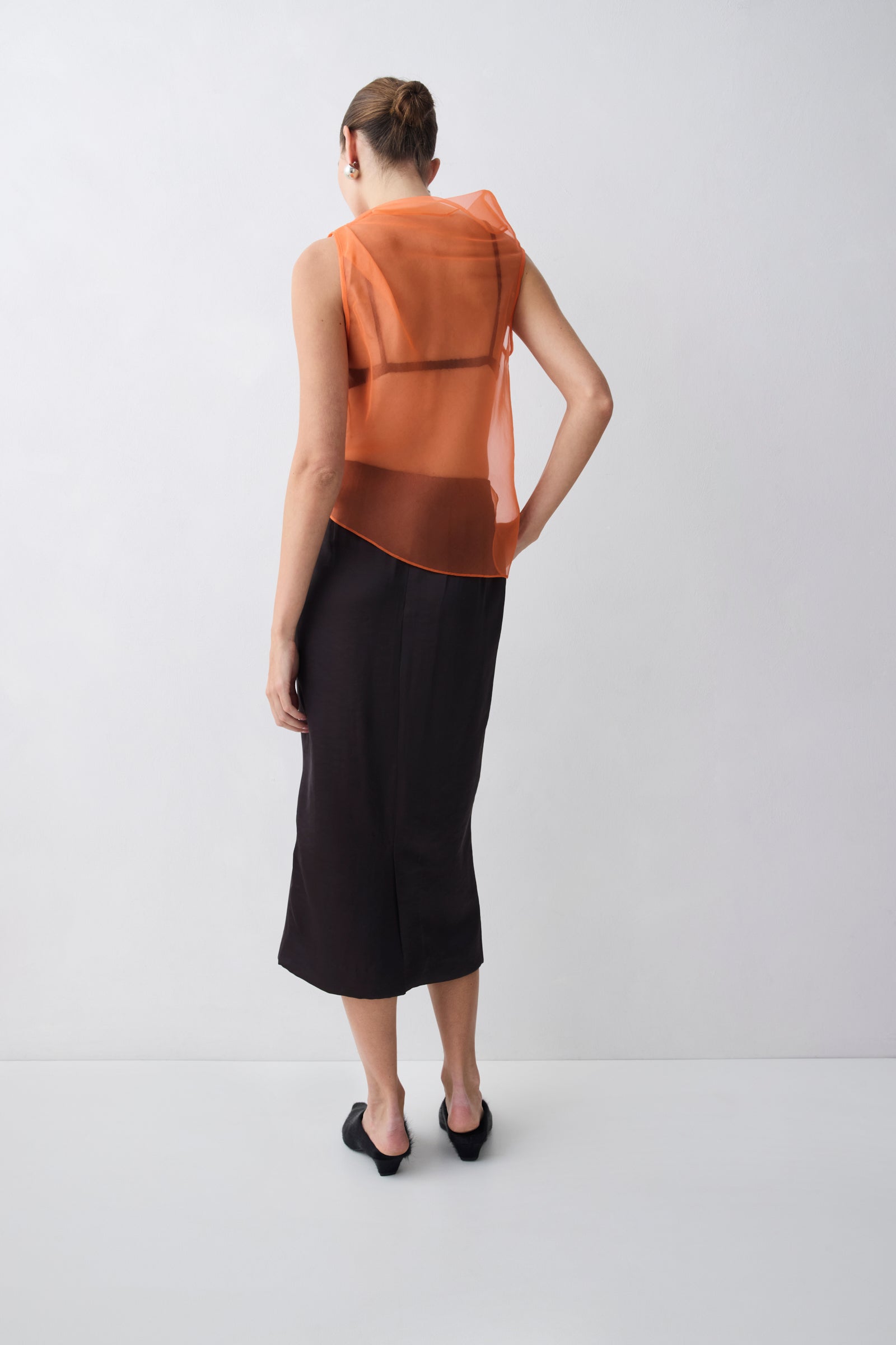 Woman wearing an orange sleeveless top and black skirt on a white background