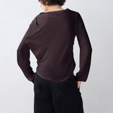 Person wearing a dark brown long-sleeve top and black pants on a white background