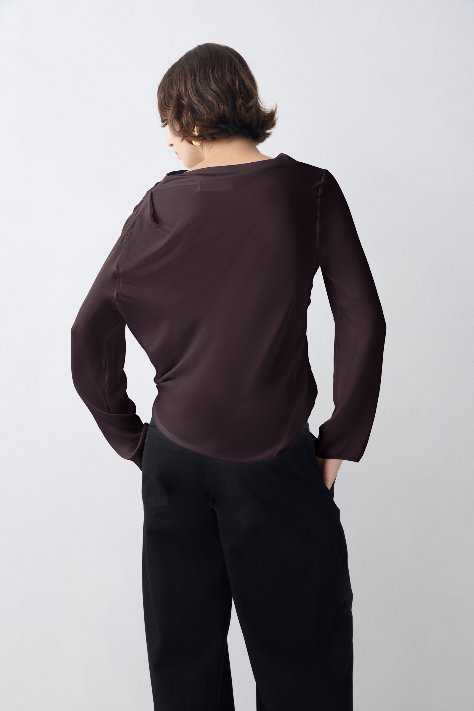 Person wearing a dark brown long-sleeve top and black pants on a white background