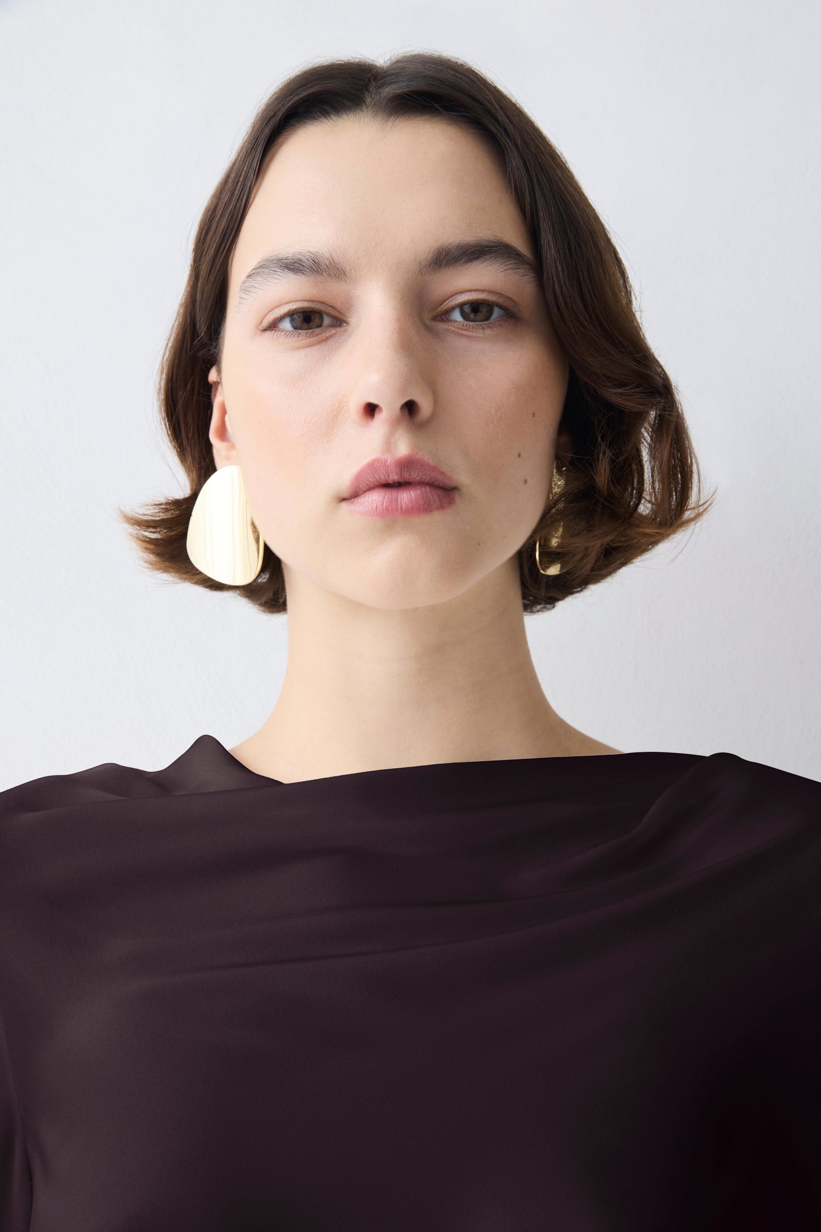 Woman wearing large earrings against a plain background