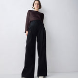 Person wearing a brown top and black wide-leg pants on a white background