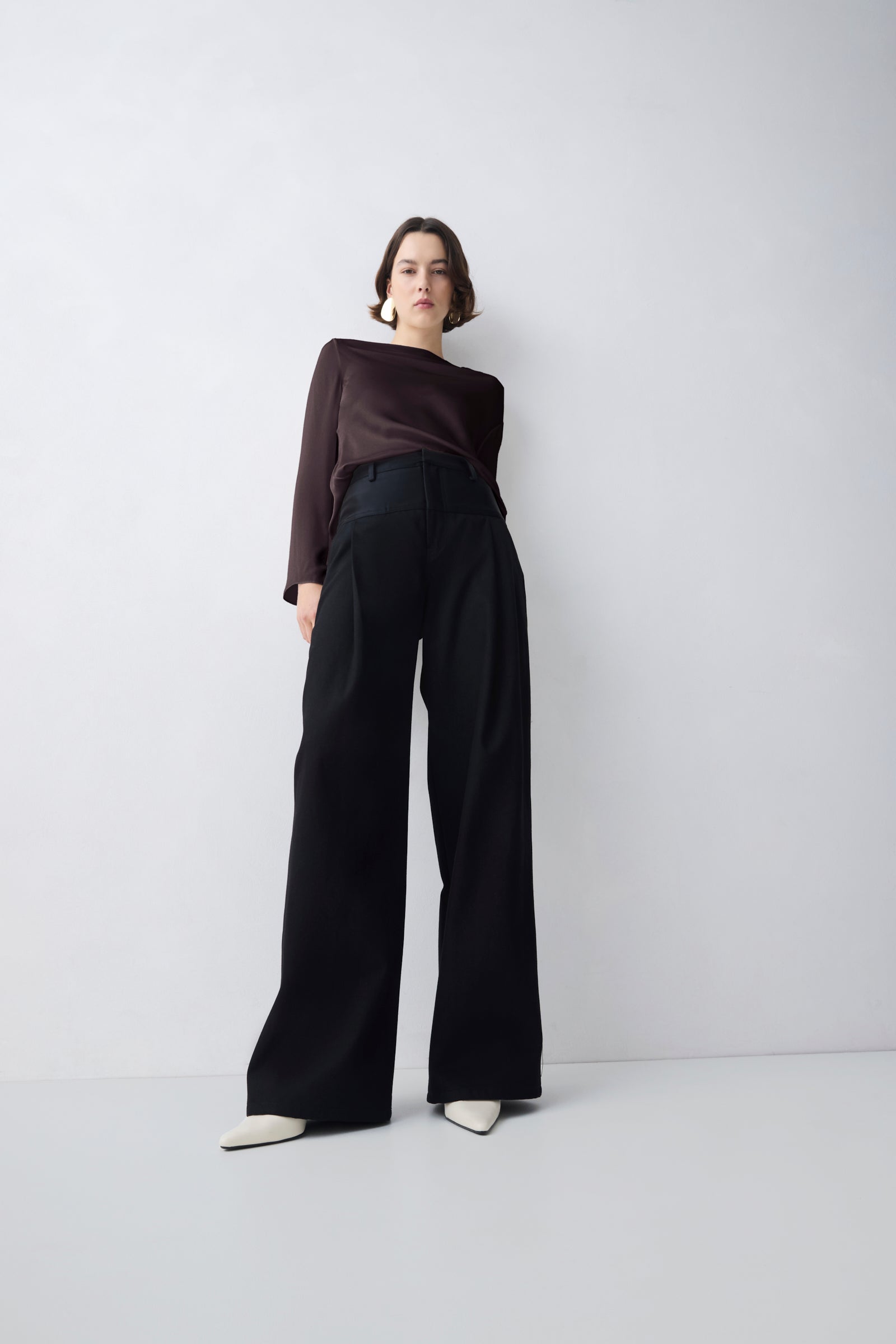 Person wearing a brown top and black wide-leg pants on a white background