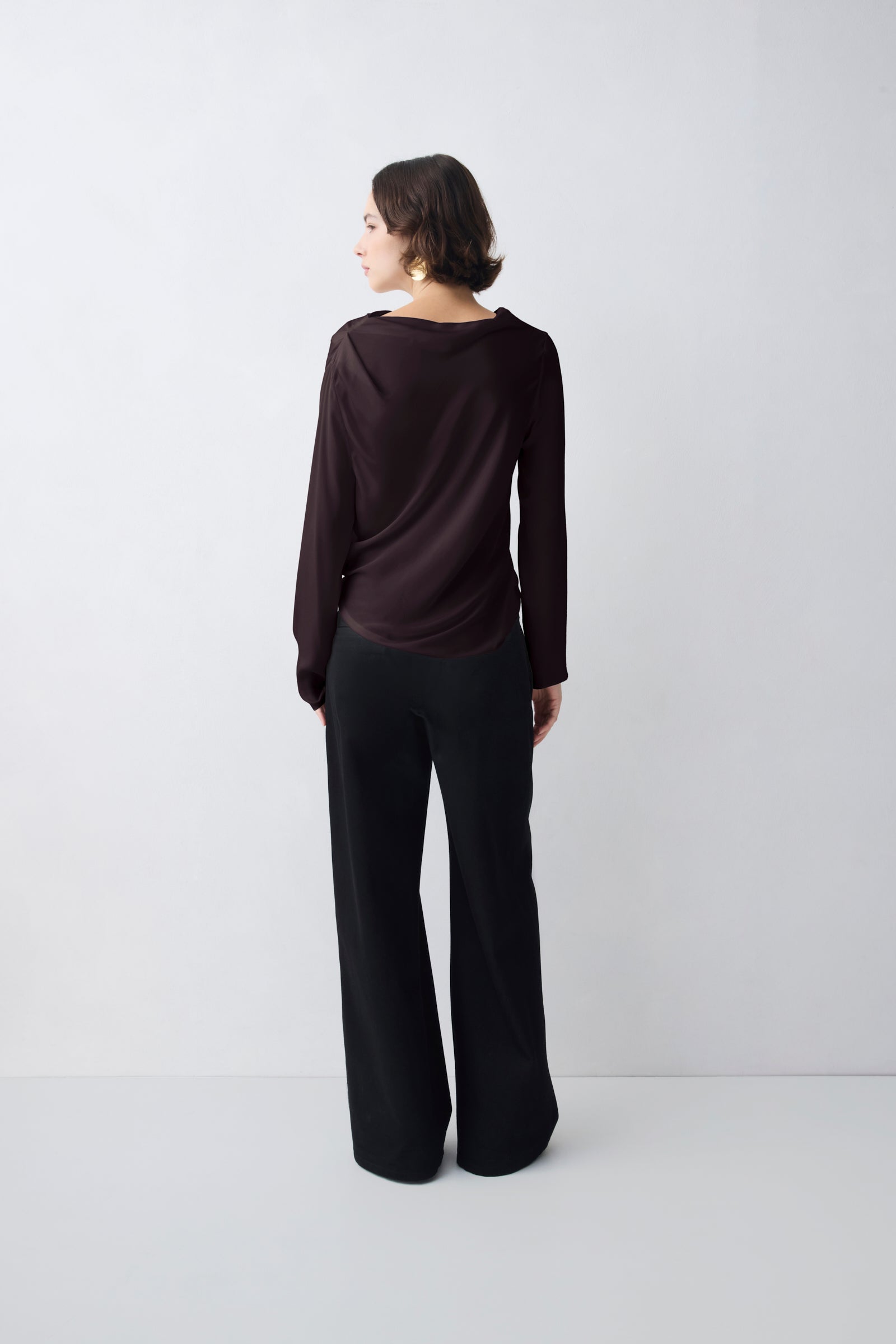 Woman wearing a dark brown long-sleeve top and black wide-leg pants on a white background