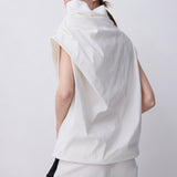 A model shown from the back wearing a sleeveless, high-waisted white top with a dramatic draped collar and matching white trousers with a black side stripe, set against a plain light gray studio background.