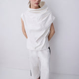 A model wearing a white draped sleeveless top and matching wide-leg trousers with black side stripes, standing against a plain white studio background.