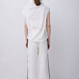 A model viewed from the back wearing a white sleeveless draped top and matching white wide-leg trousers with black side stripes, paired with black high-heeled sandals, against a plain light gray studio background.