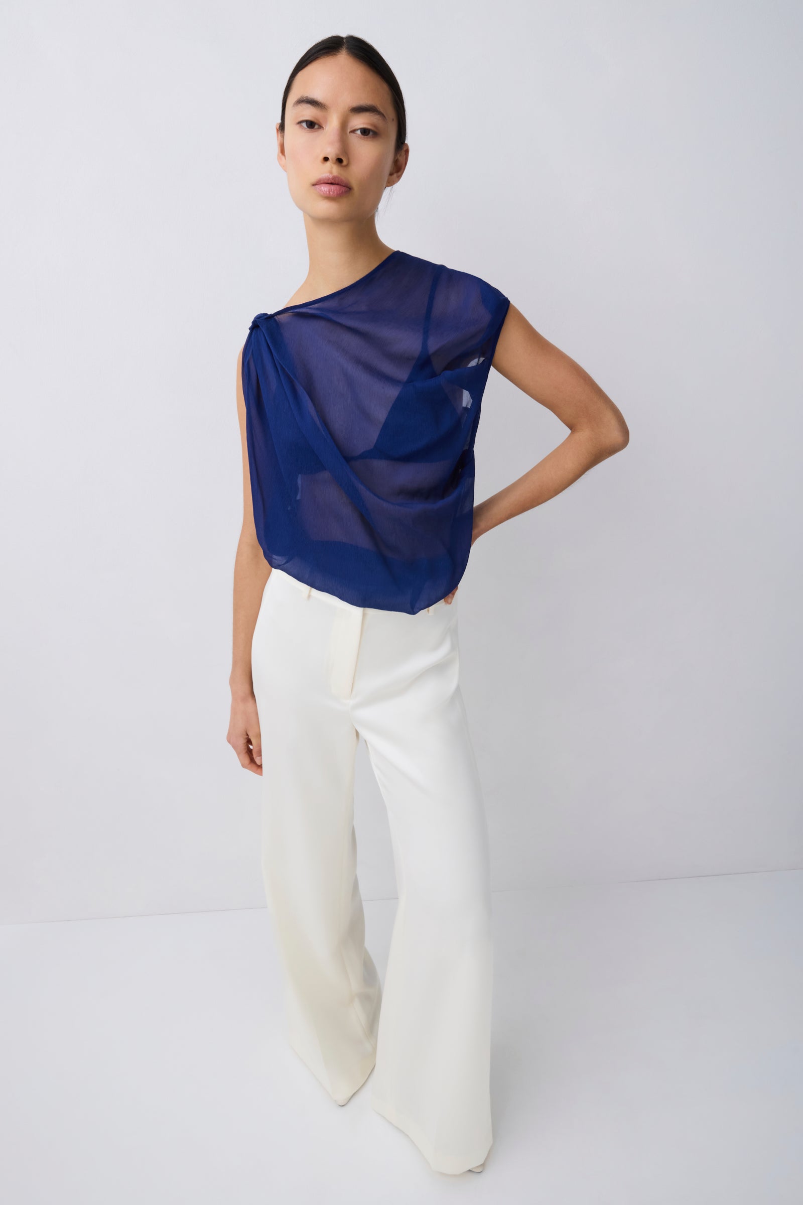 Woman wearing a blue top and white pants on a light gray background