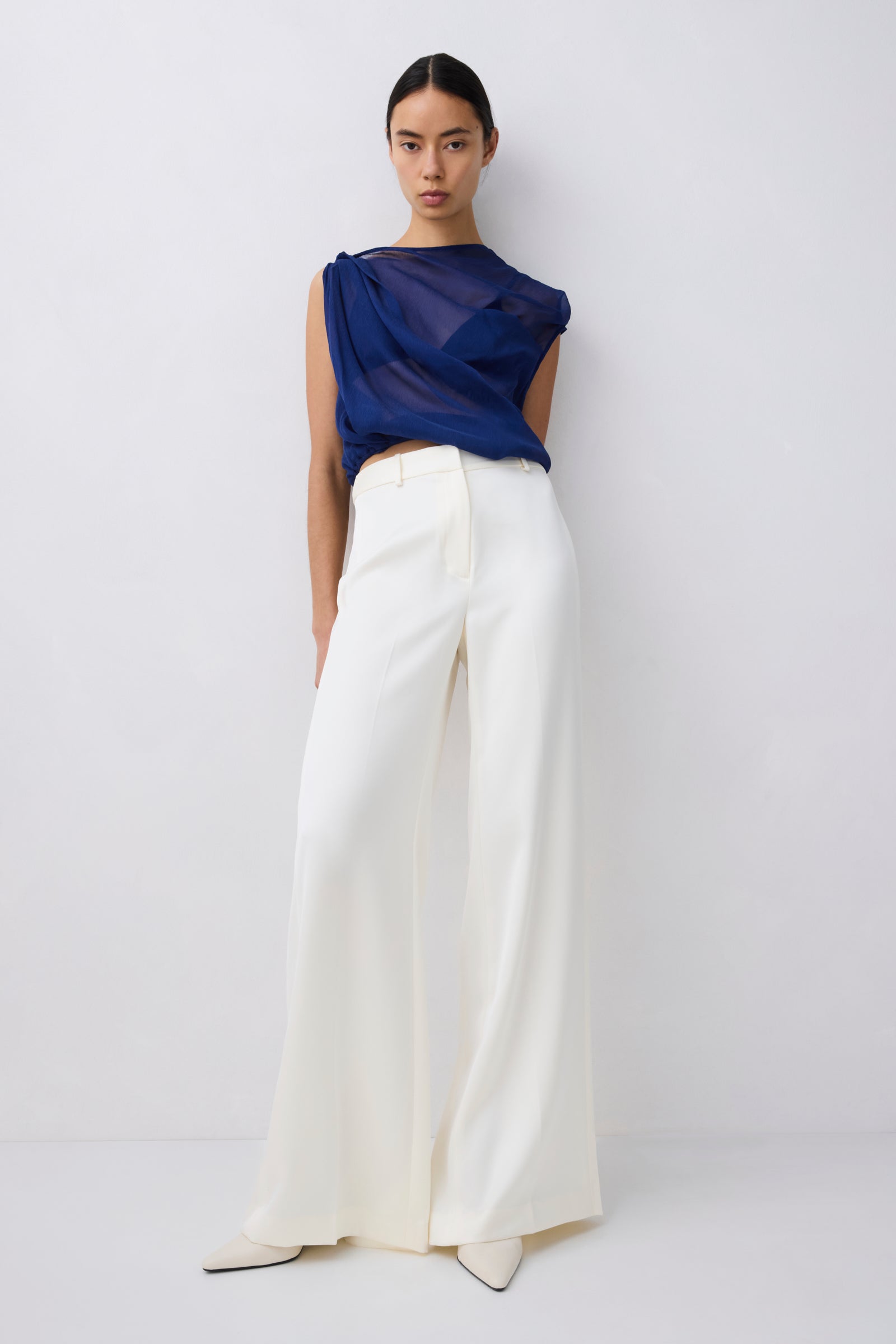 Woman wearing a blue top and white pants on a plain background