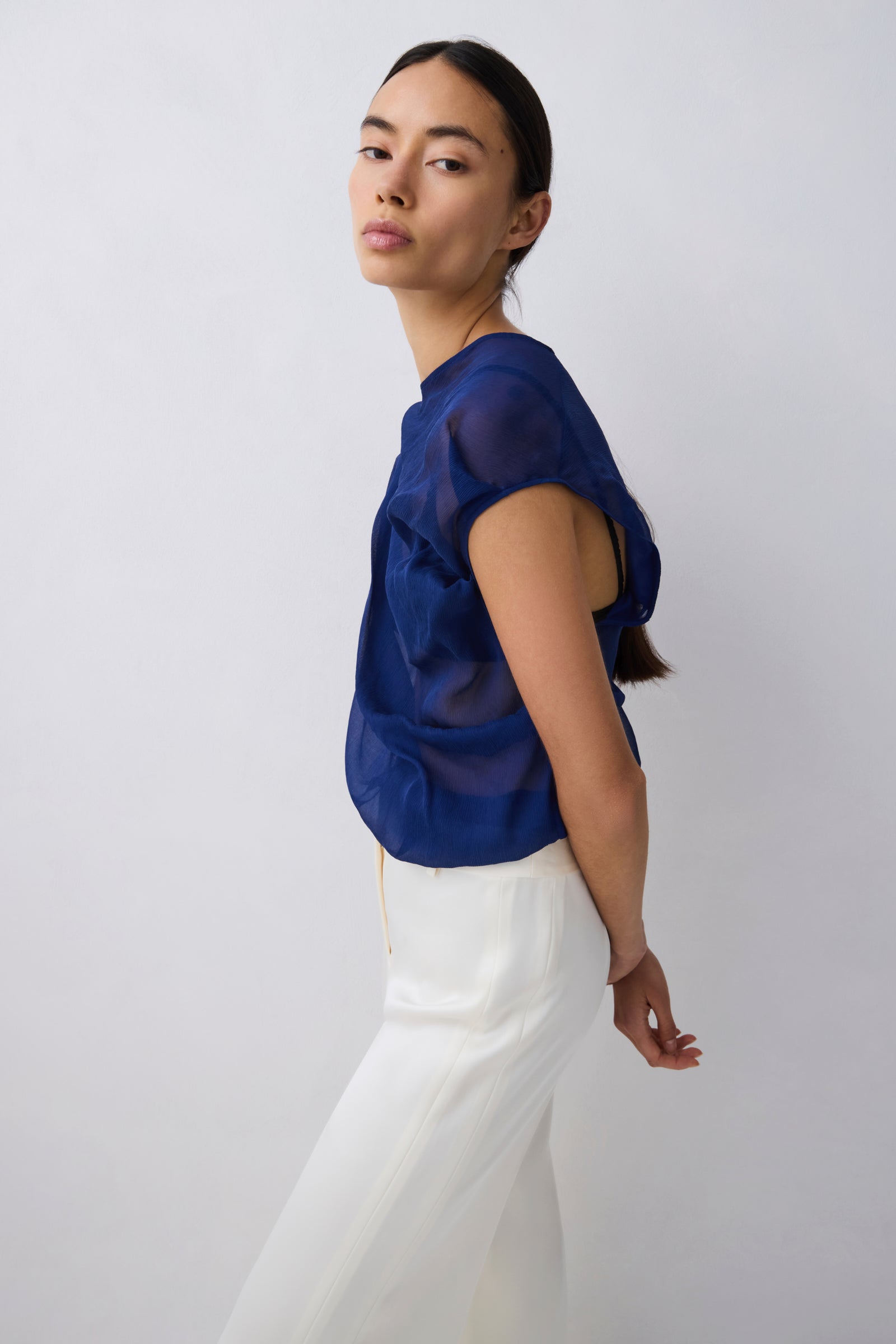 Woman wearing a blue top and white pants against a plain background