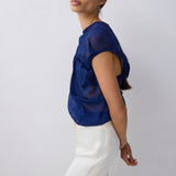 Woman wearing a blue top and white pants against a plain background
