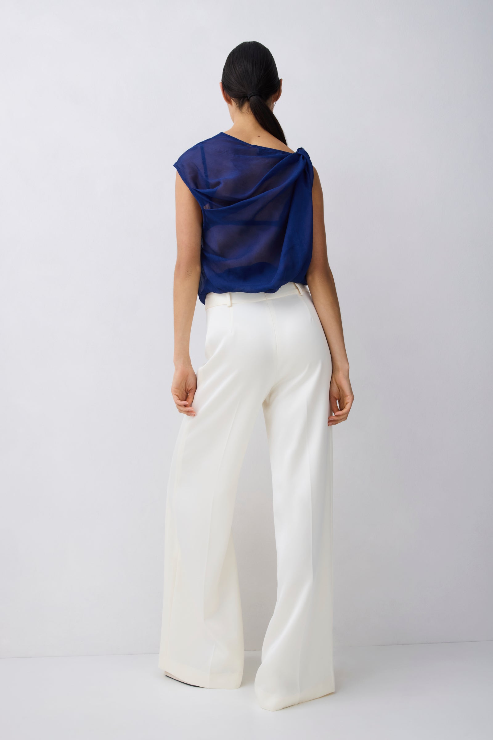 Person wearing a blue top and white pants on a plain background