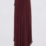 A woman wearing a deep burgundy off-the-shoulder maxi dress with a flowing skirt, shown from the back against a light gray studio background.