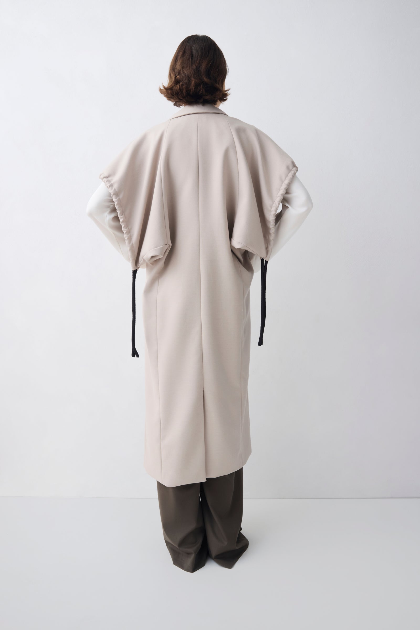 Person wearing a long beige coat on a white background