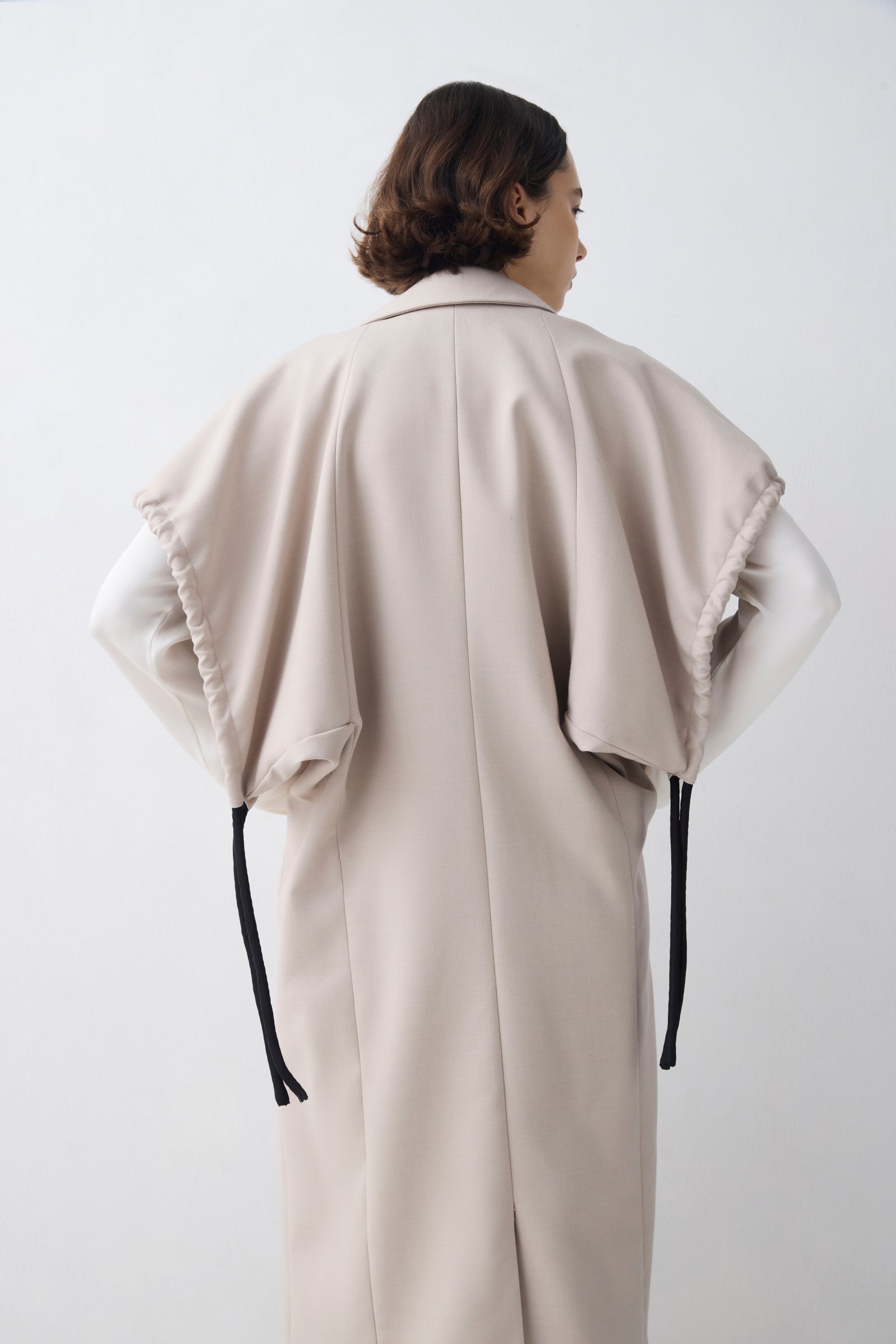 Person wearing a beige poncho with black straps on a white background
