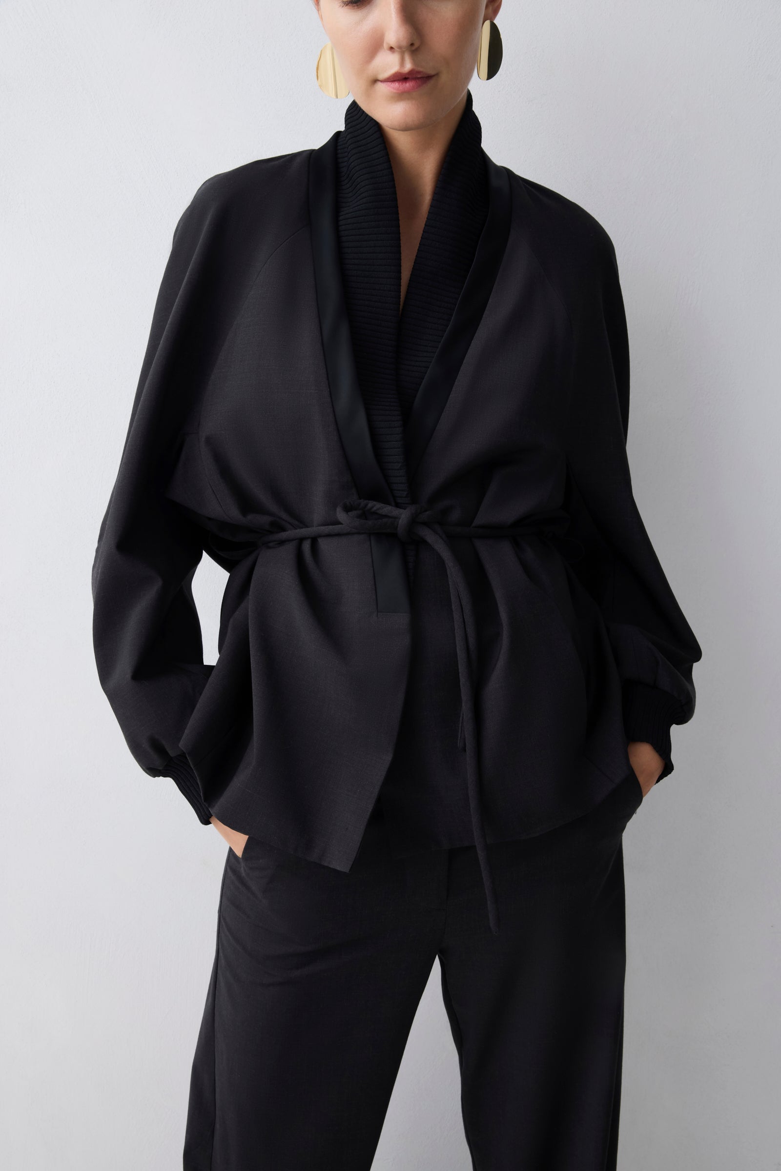 Person wearing a black outfit with a belt against a white background