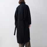 Person wearing a black coat and gray pants on a white background