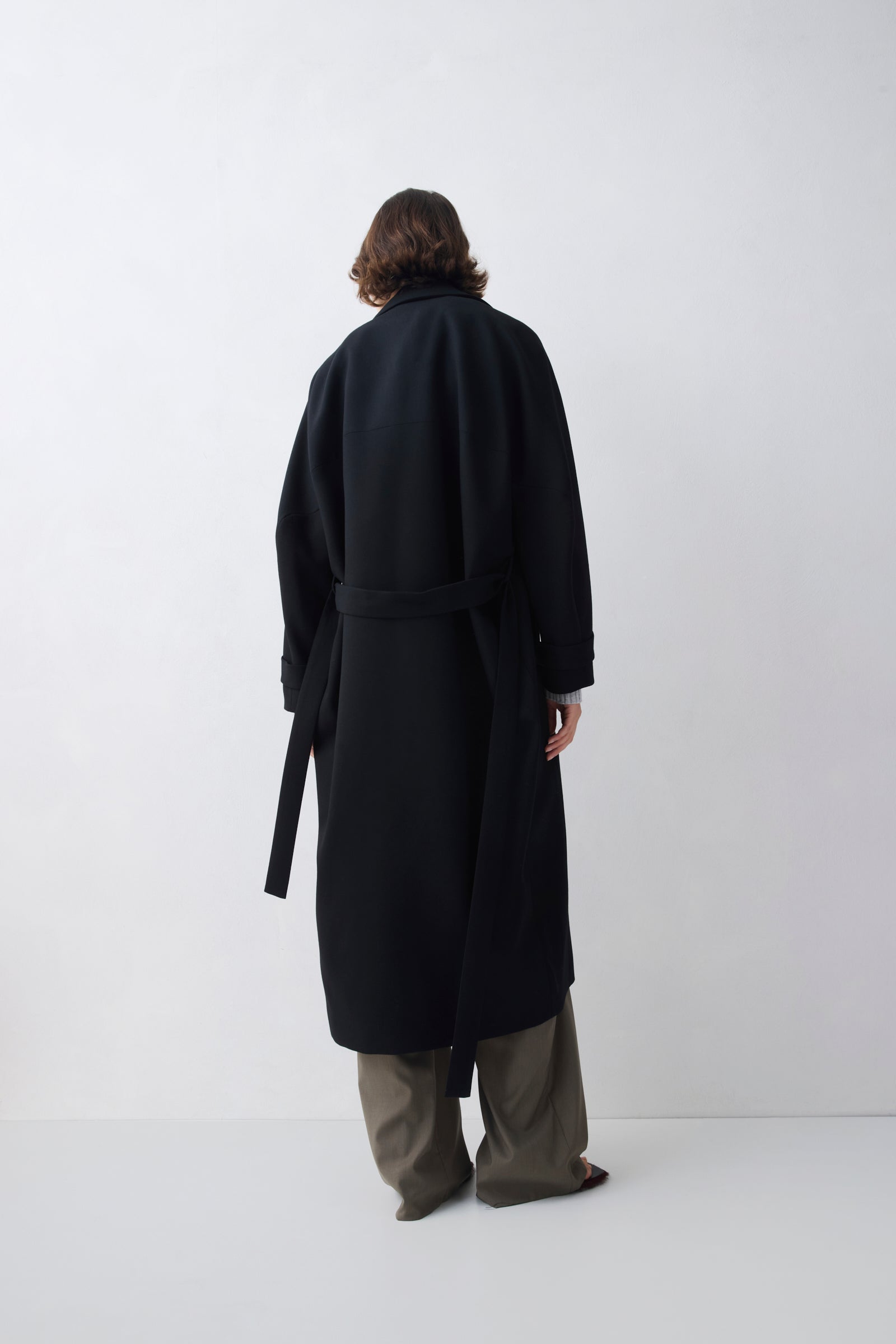 Person wearing a black coat and gray pants on a white background