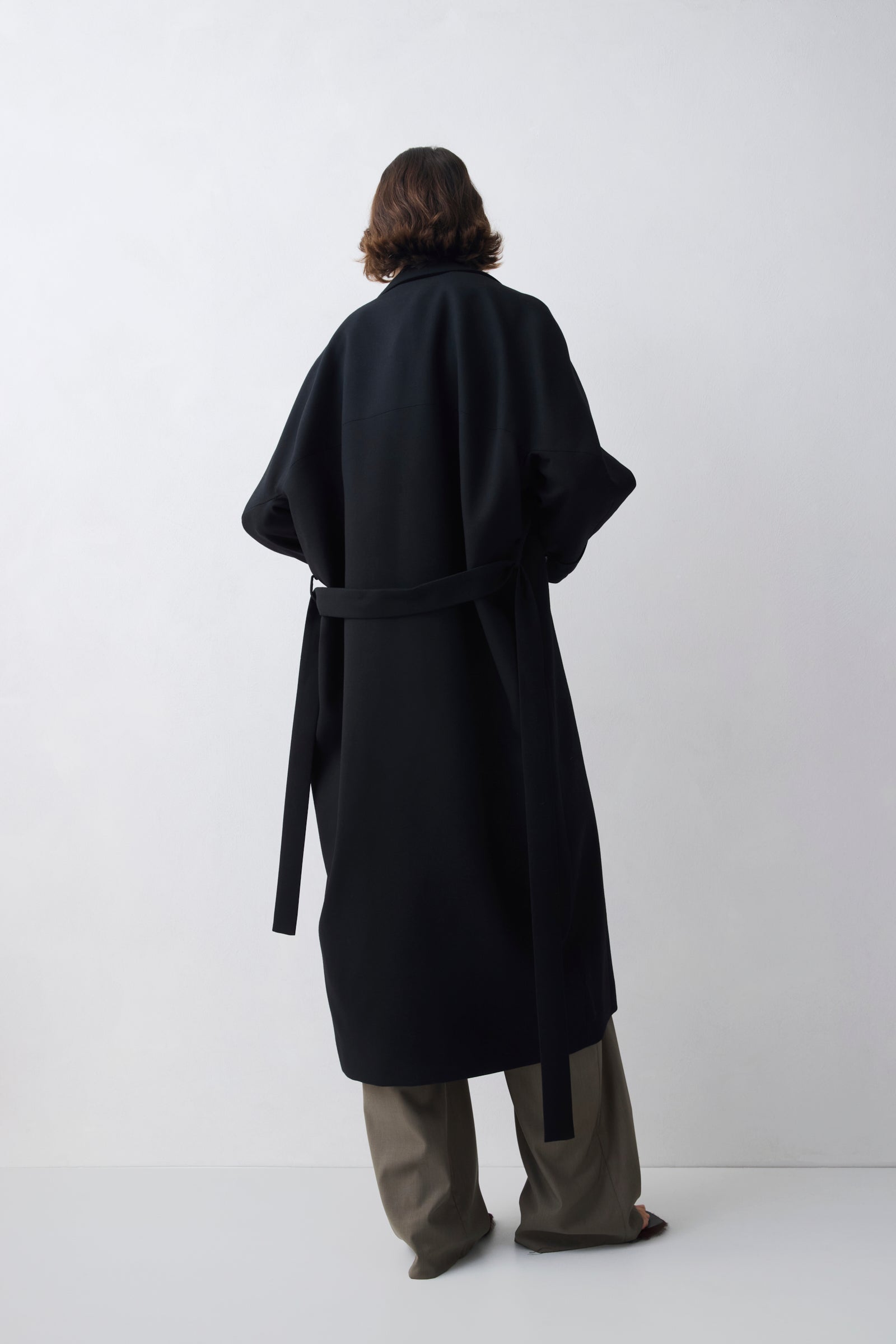 Person wearing a black coat from behind on a white background