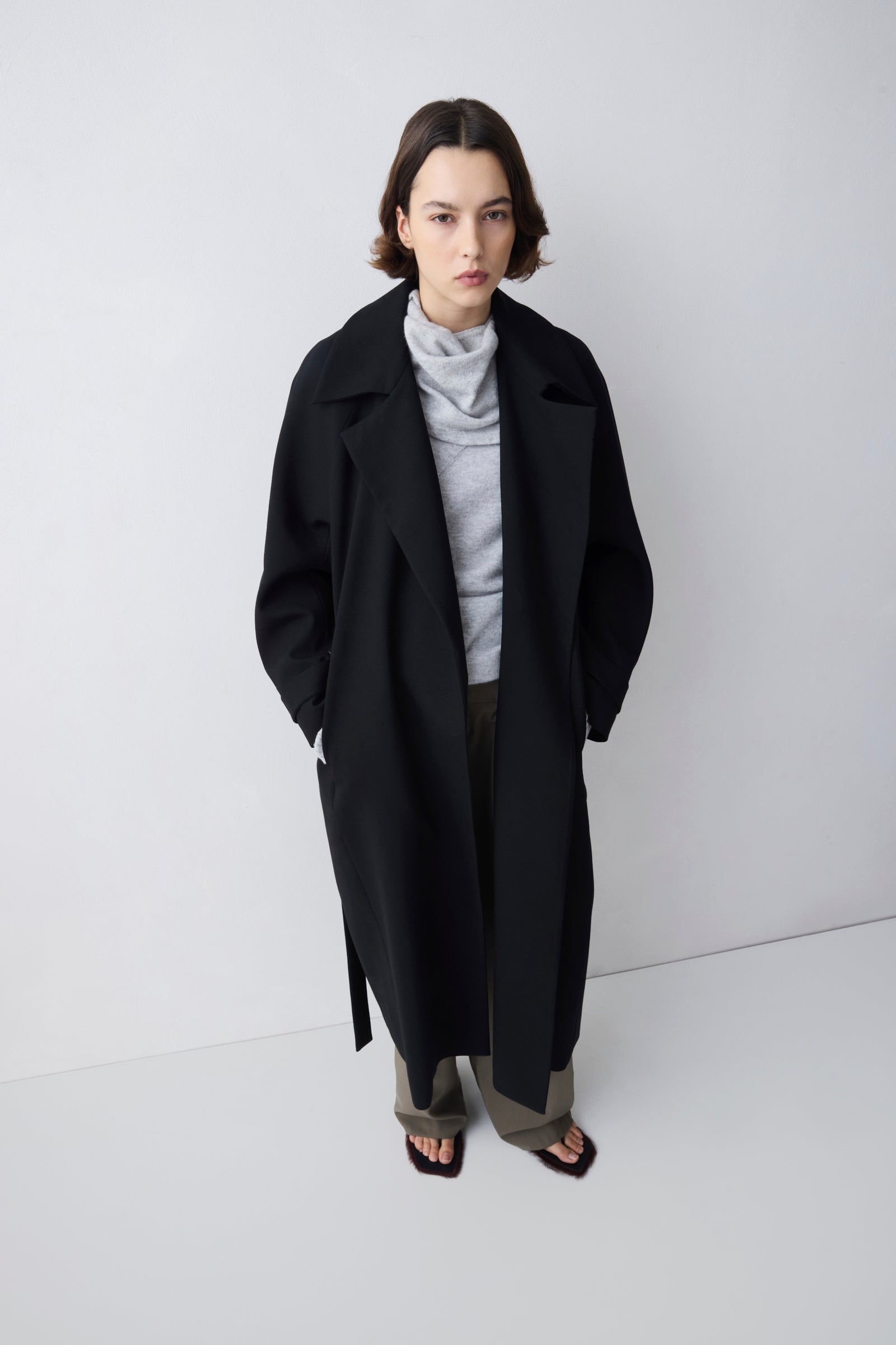 Person wearing a black coat and gray outfit on a white background