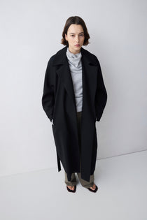 Person wearing a black coat and gray outfit on a white background