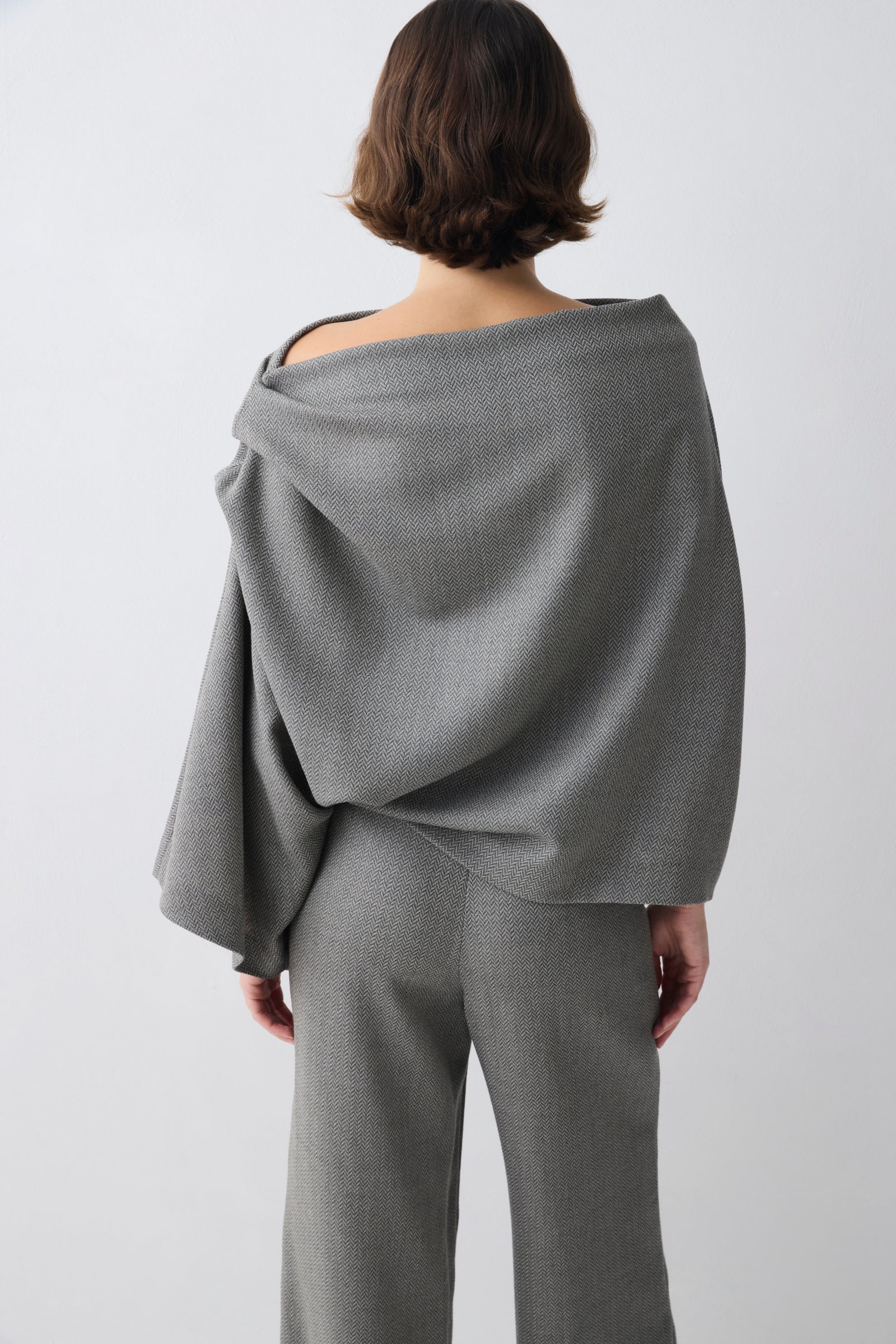 Person wearing a gray off-shoulder top and pants on a white background