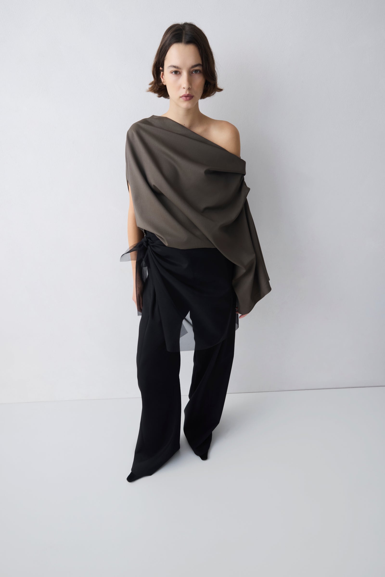 Woman wearing a draped brown top and black pants on a white background