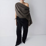 Woman wearing a draped brown top and black pants on a white background