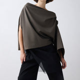 Woman wearing a draped brown top and black pants on a white background