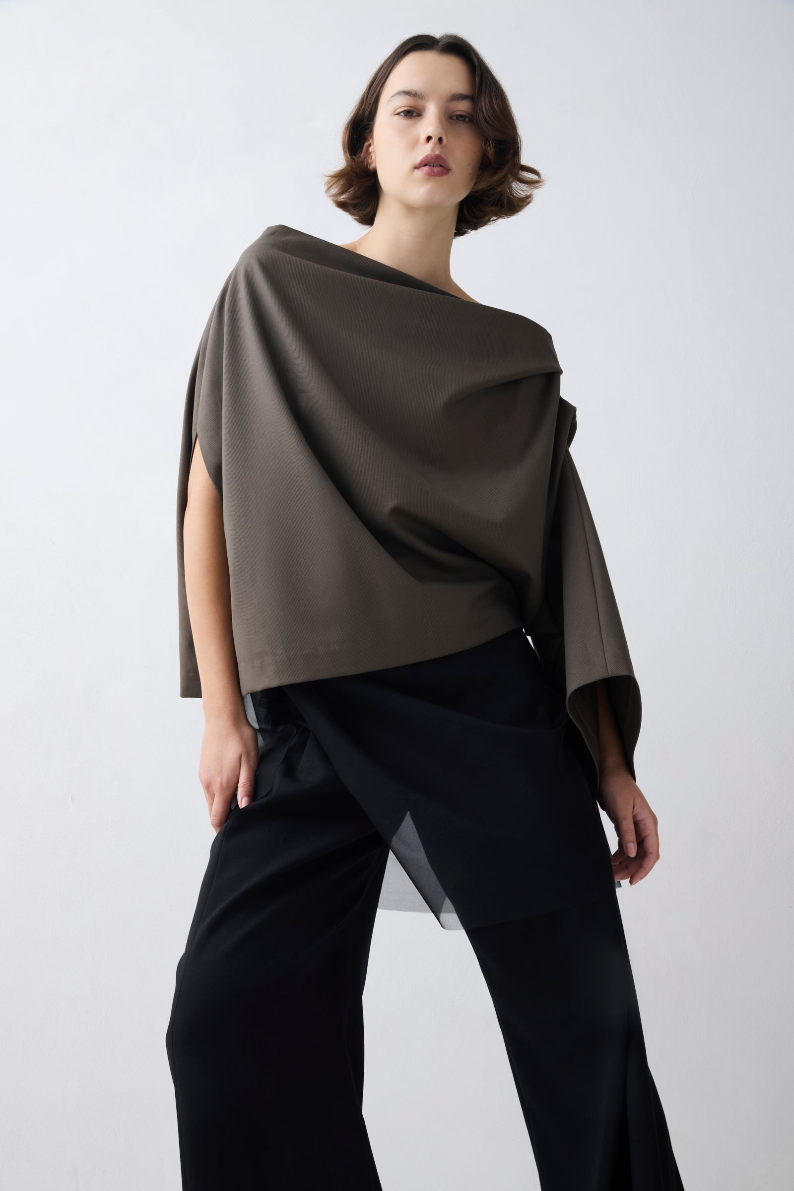 Woman wearing a draped brown top and black pants on a white background