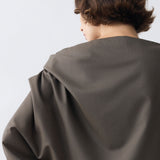 Person wearing a large, dark gray fabric draped over their shoulders against a light background