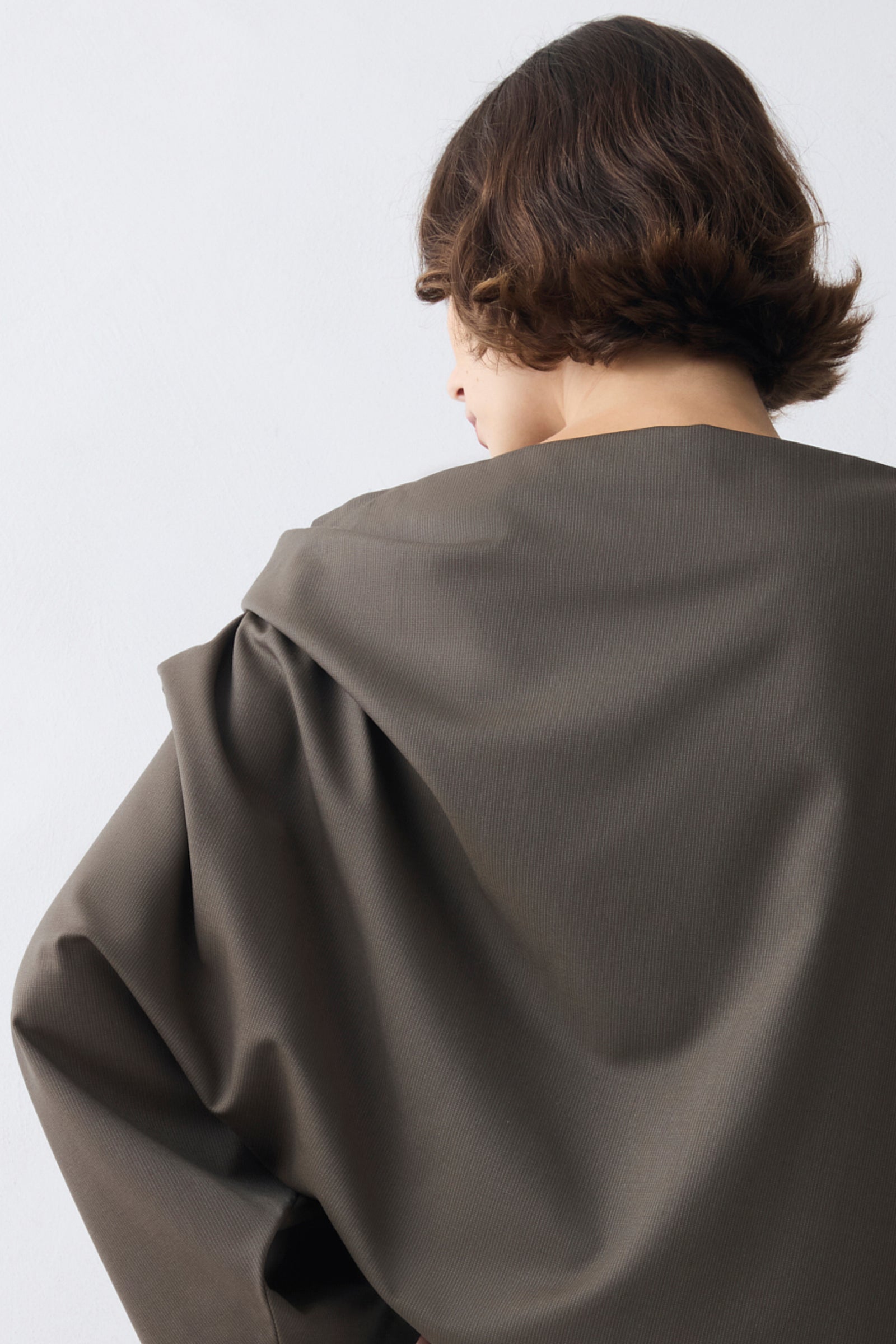 Person wearing a large, dark gray fabric draped over their shoulders against a light background