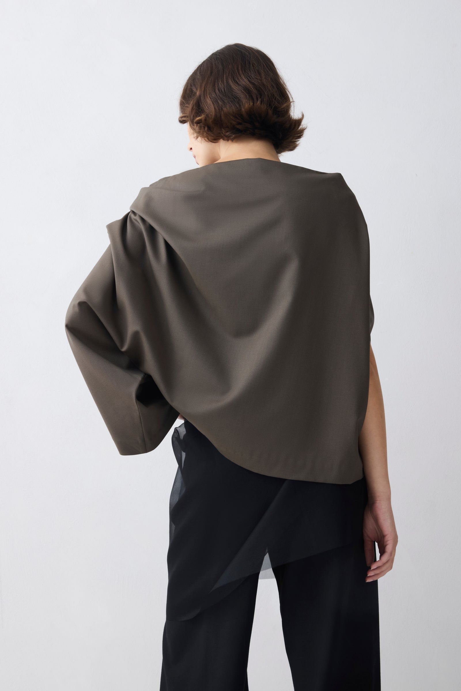 Person wearing a dark green cape over a plain background