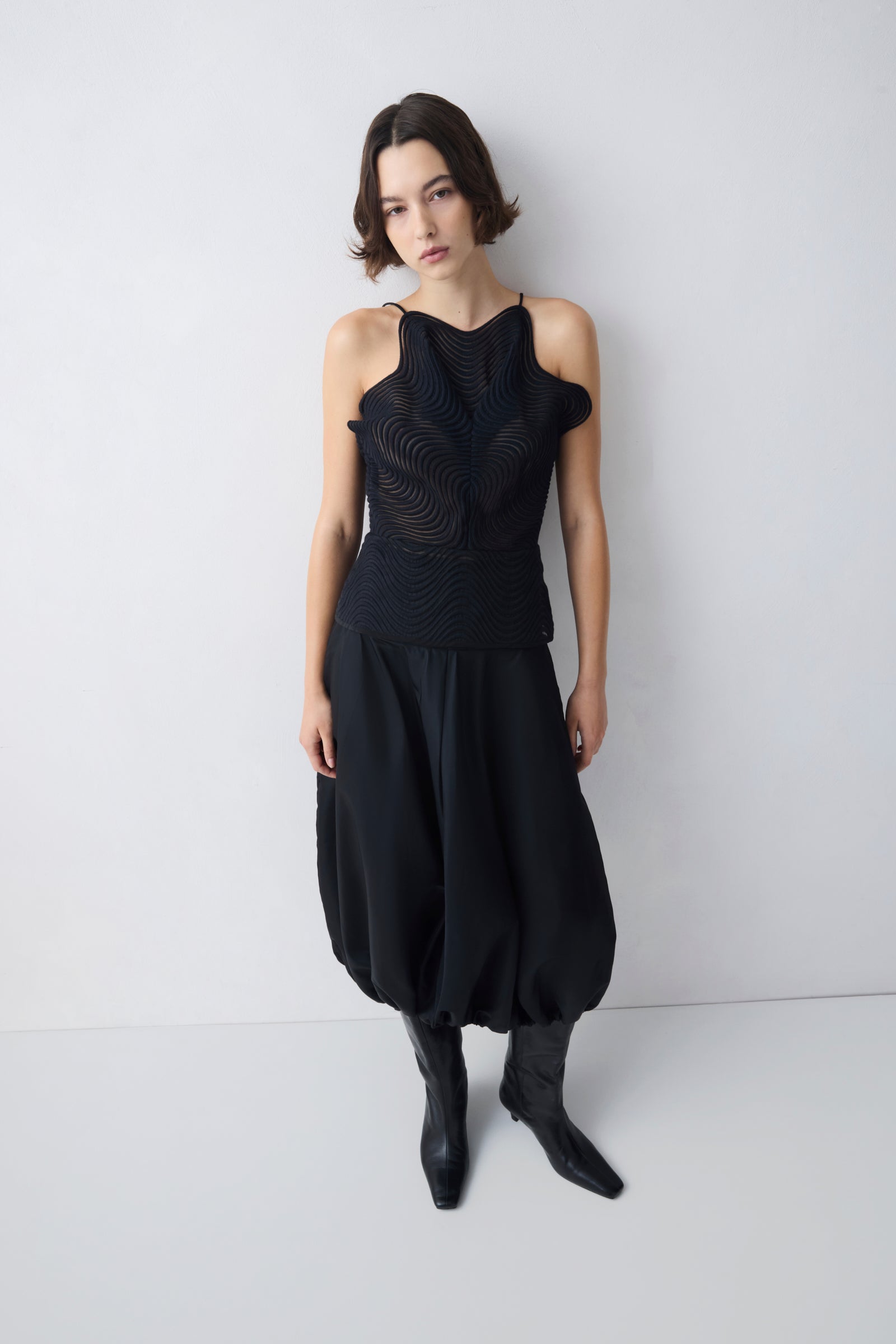 Woman wearing a black sleeveless top and skirt with black boots against a white background
