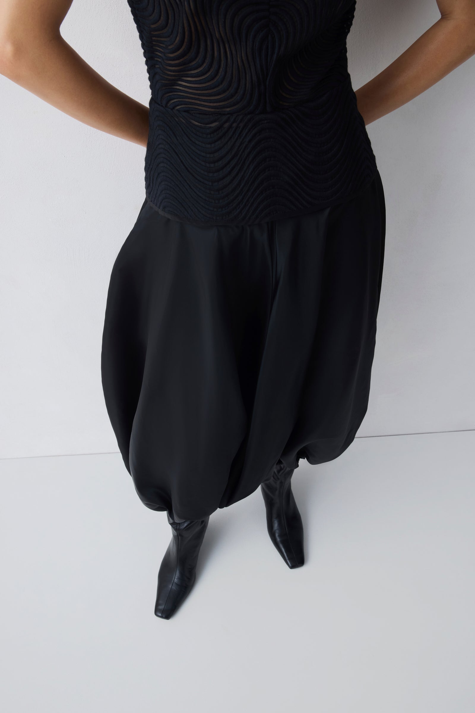 Person wearing a black dress with wide-leg pants and black shoes on a white background