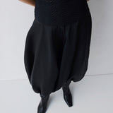Person wearing a black dress with wide-leg pants and black shoes on a white background