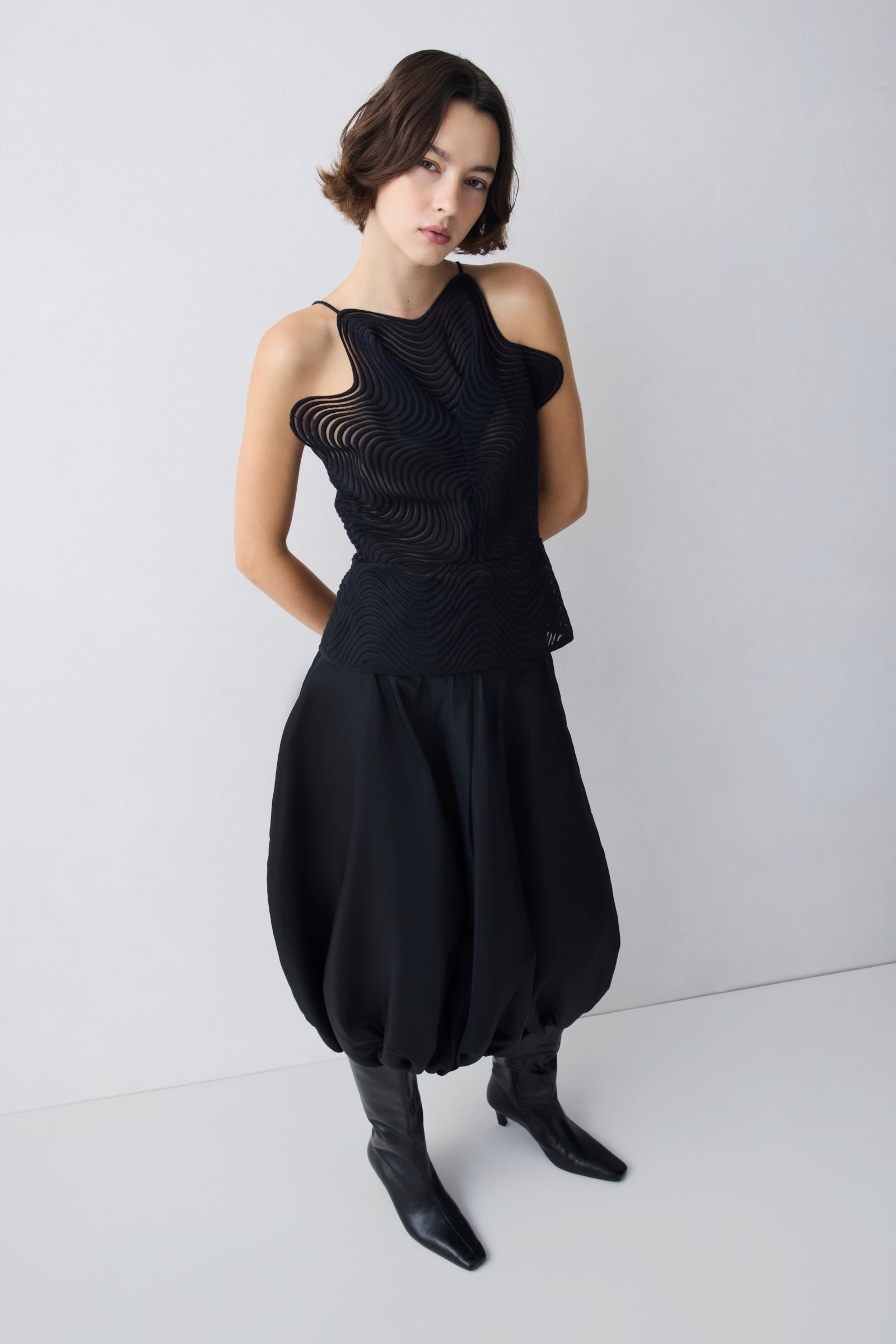 Woman wearing a black sleeveless top and black pants on a white background