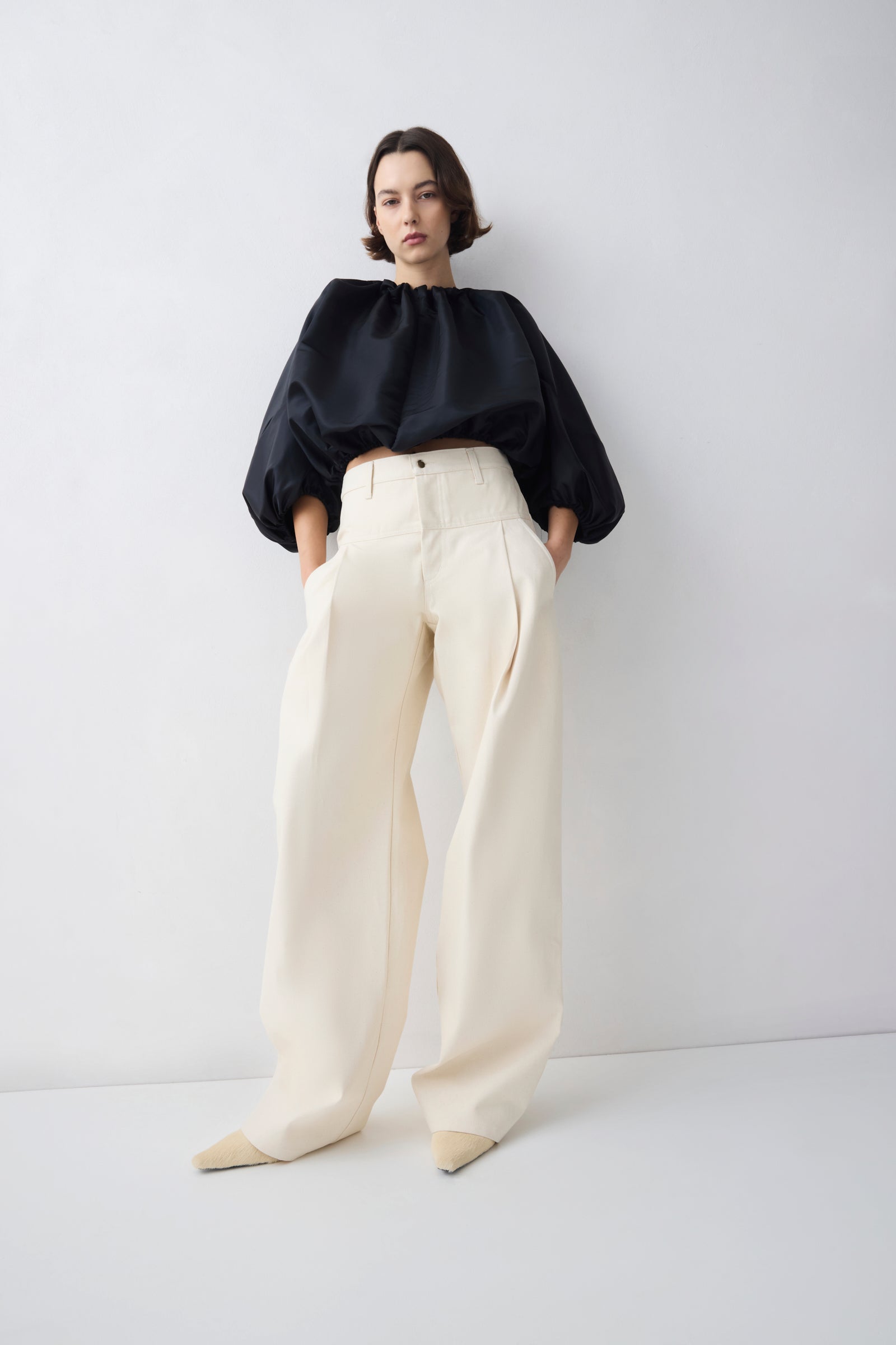 Person wearing a black top and white pants on a white background