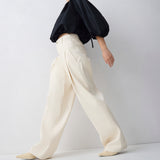 Person wearing a black top and white pants on a light gray background