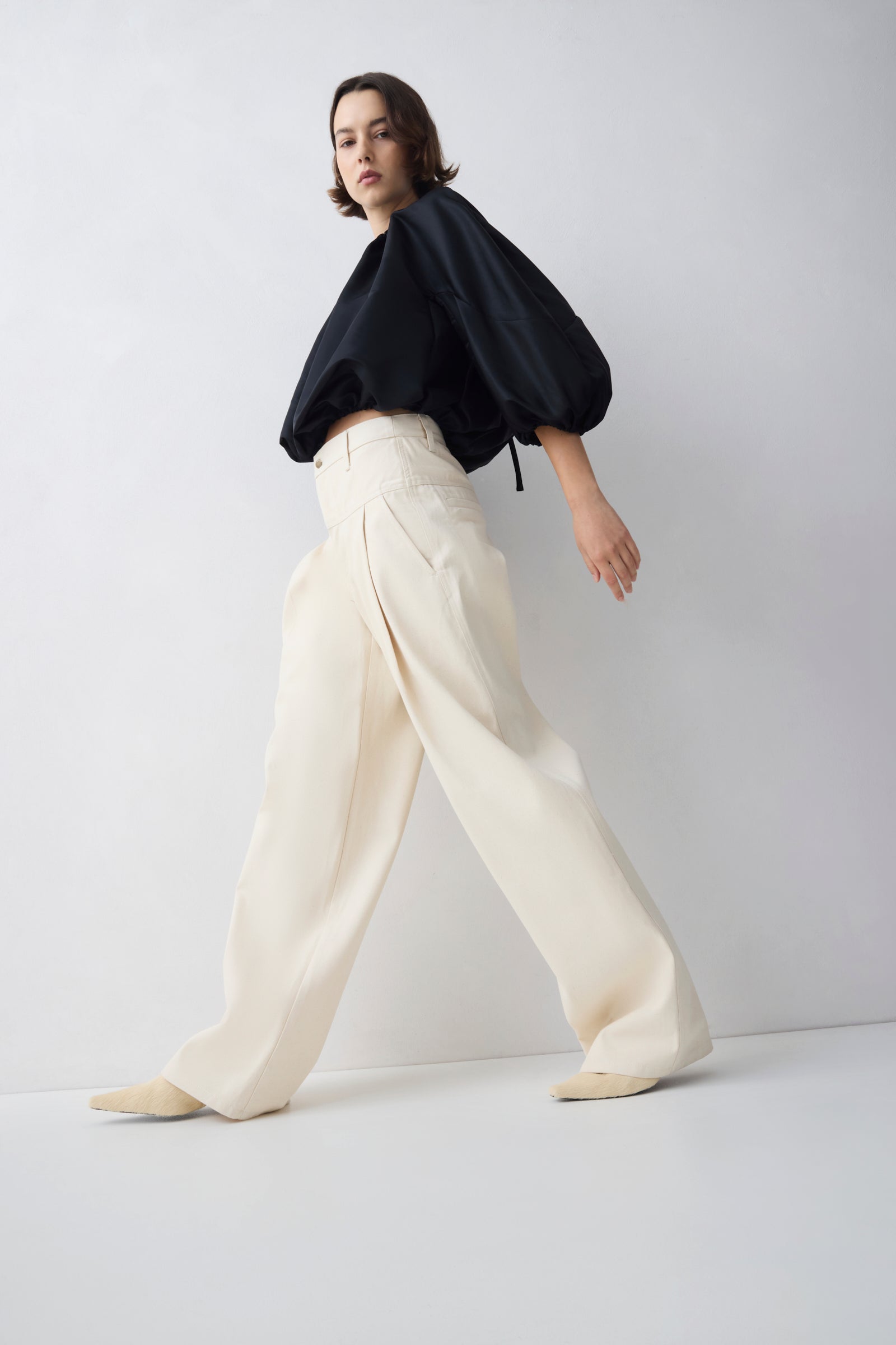 Person wearing a black top and white pants on a light gray background