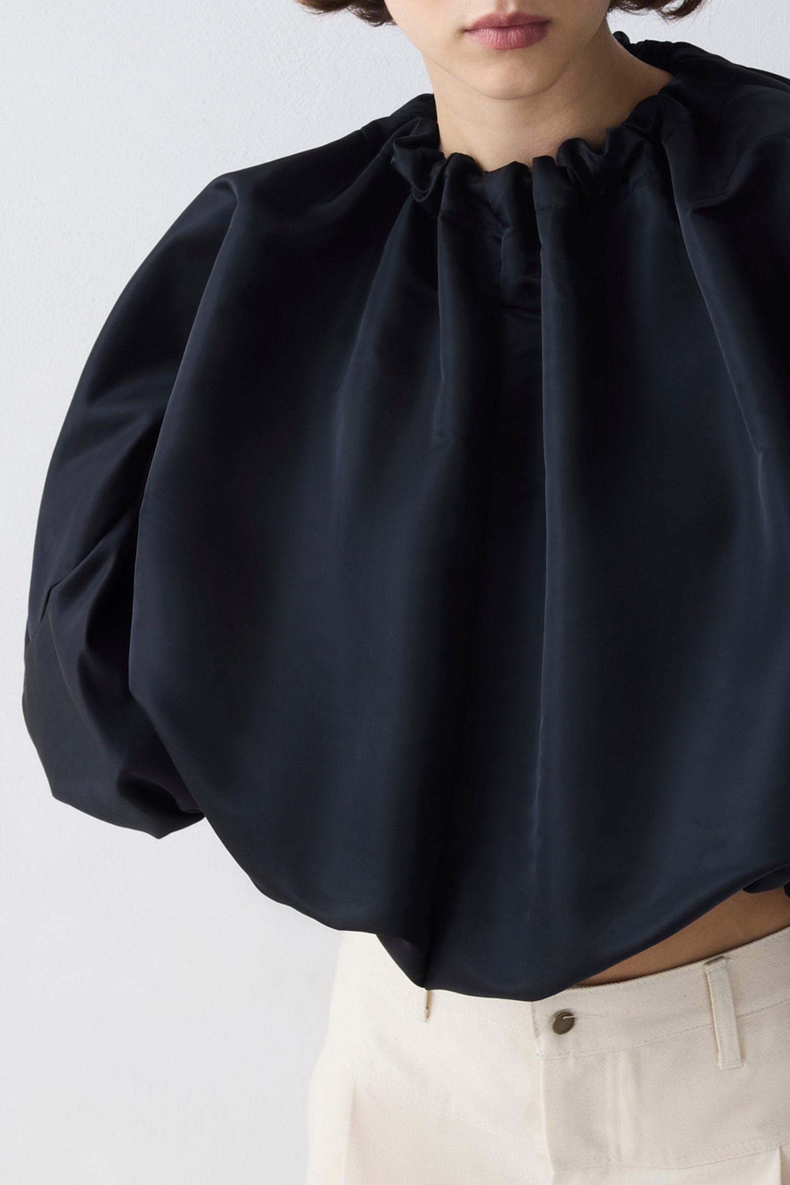 Black blouse with puffed sleeves worn by a person on a light gray background