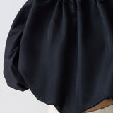 Black blouse with puffed sleeves worn by a person on a light gray background