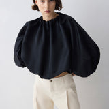 Woman wearing a black blouse with puffed sleeves and beige pants on a white background