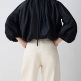 Person wearing a black blouse with balloon sleeves and white pants on a light gray background