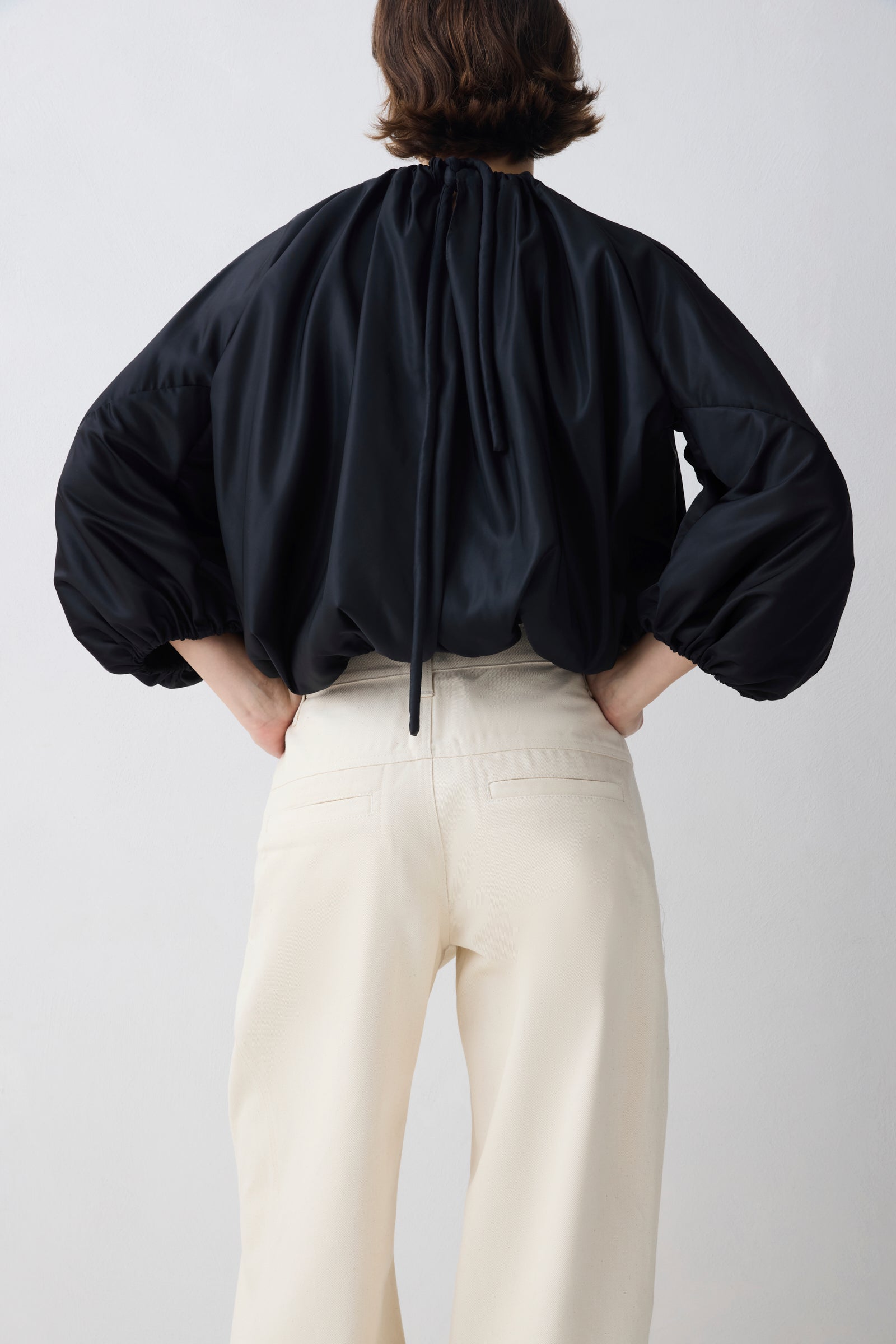 Person wearing a black blouse with balloon sleeves and white pants on a light gray background