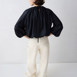 Person wearing a black blouse and white pants on a plain background