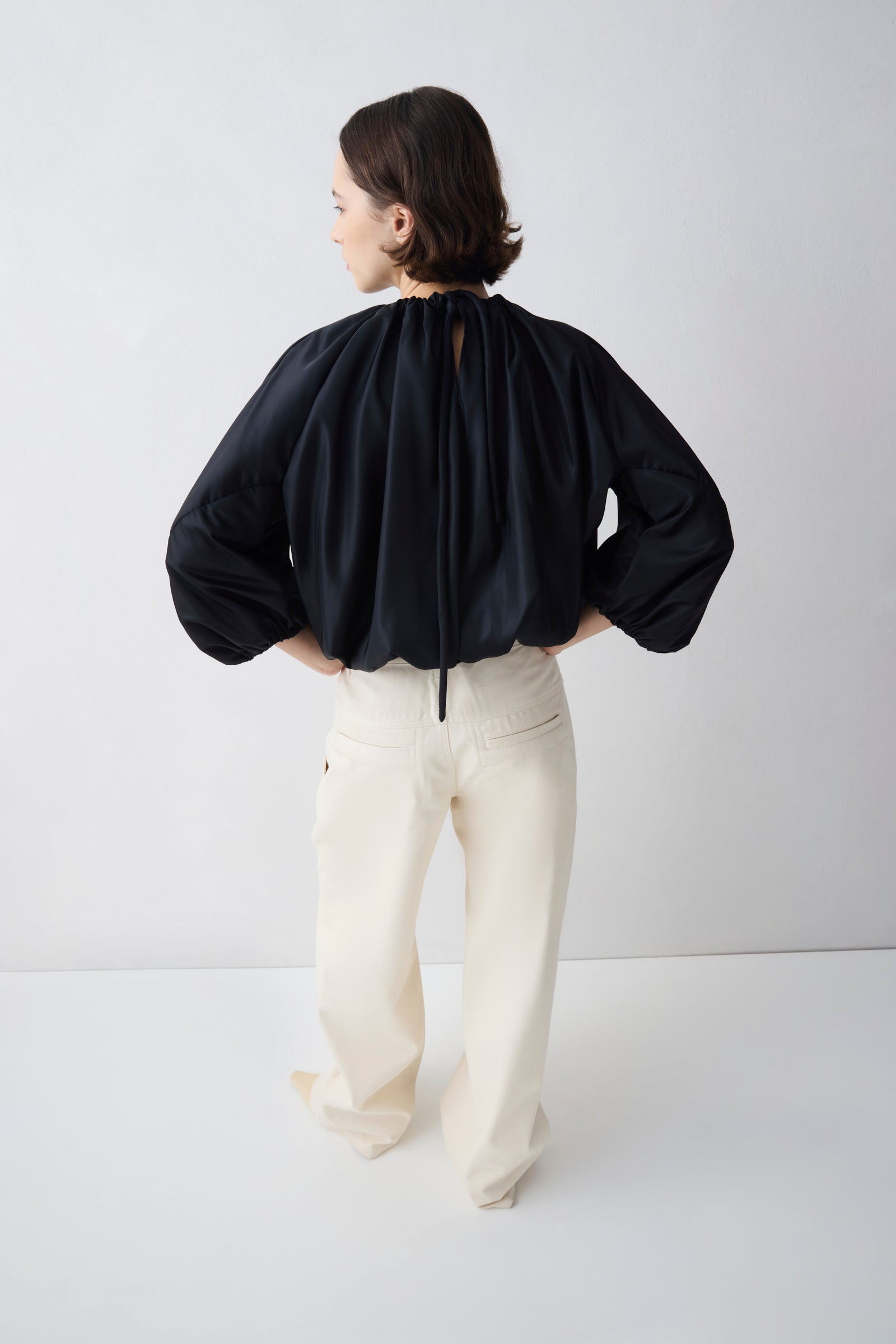 Person wearing a black blouse and white pants on a plain background