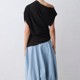 Person wearing a black one-shoulder top and light blue skirt on a white background
