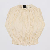 A cream-colored, crinkled cotton blouse with voluminous balloon sleeves and a gathered elastic hem, laid flat against a light gray background.